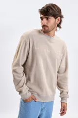 Buzo de polar color taupe con cuello redondo, puños y ruedo acanalados. Presenta una estampa sutil en el pecho con texto decorativo.