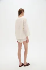 Blusa de algodón blanco con diseño de broderie, cuello en V y cierre con lazos frontales, mangas largas de corte holgado.