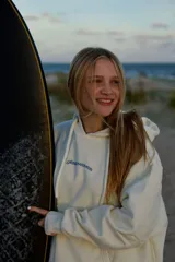 Hoodie blanco con capucha y canguro, estampado en la espalda con el texto "RIDE glassywaves" en azul claro, acompañado de un gráfico de olas y texto pequeño debajo.