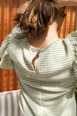 Blusa de spandex con estampado vichy en tonos pistacho y blanco, con mangas al codo adornadas con tres volados y puños elásticos. Cierre con botón en la parte posterior.