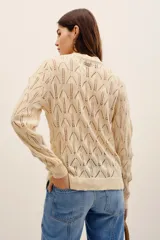Cardigan de punto color beige con escote en V, cierre frontal con botones y detalles de flores bordadas en relieve a lo largo de la abertura. Cuenta con mangas largas y terminaciones en rib.