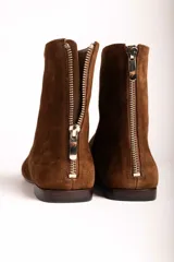 Botas cortas de gamuza color marrón, con punta cuadrada y cierre lateral. Diseño minimalista con costura central vertical.