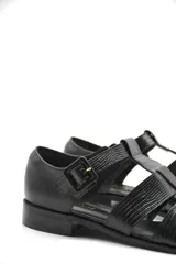 Zapato tipo cangrejera de cuero color marrón, con diseño de tiras entrelazadas, punta cerrada y pulsera con hebilla ajustable al tobillo. Cuenta con un taco bajo de madera.