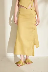 Falda midi de lino color mostaza, con corte asimétrico, abertura lateral y detalle de botones de madera con bordados alusivos.