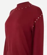 Suéter de punto color bordó con cuello alto y mangas largas con puños ajustados. Presenta aplicaciones de tachuelas metálicas decorativas en el escote y a lo largo de las mangas.
