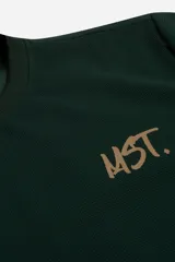 Remera de manga corta color verde oscuro con textura tipo waffle. Presenta un estampado pequeño en el pecho con las siglas 'MST.' en color beige y un estampado de mayor tamaño en la espalda. Posee cuello redondo acanalado y corte regular.