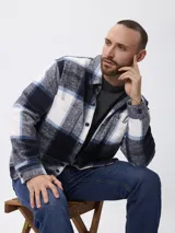 Sobrecamisa de corte recto con estampado de cuadros en tonos azul, blanco y gris. Presenta cuello clásico, cierre frontal con botones, mangas largas con puños abotonados y bolsillos frontales en el pecho.