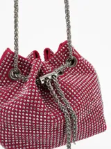 Cartera tipo bucket bag de color rojo, completamente cubierta de strass plateado. Presenta un cierre de cordón ajustable con cadena metálica plateada y una correa larga de cadena para llevar al hombro o cruzada.