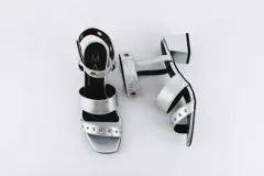 Sandalias negras de cuero con dos tiras horizontales sobre el pie y pulsera al tobillo con ojalillos y tachas. Taco cuadrado de 5 cm.