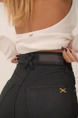 Jean de tiro alto color negro con acabado encerado, silueta slim y pierna levemente evasé.