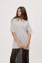 Remera oversized de manga corta y cuello redondo, de color negro con efecto acid wash y aplicación de strass en la parte superior.