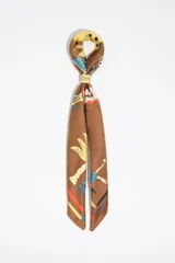 Pañuelo marrón con estampado colorido y detalles gráficos, confeccionado en poliéster reciclado, con hebilla metálica dorada decorativa.