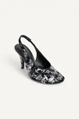 Zapato de tacón destalonado con abalorios y lentejuelas en tonos negros y plateados, escote redondo, punta redonda y tacón fino alto.