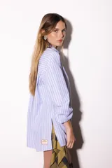 Camisa oversize a rayas celestes y blancas, con cuello camisero, manga larga y hilera de botones dorados metálicos.