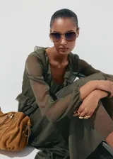 Vestido midi color verde militar, confeccionado en tejido fluido de poliéster. Presenta un diseño evasé, escote de pico con volantes, y mangas largas con puños elásticos. Incluye detalles de volantes en el cuello y forro interior.
