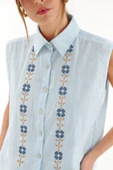 Chaleco camisero de algodón color celeste, sin mangas, con cuello camisero, botonadura frontal y detalles de bordado en punto cruz a lo largo del frente.