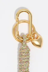 Llavero con cabo de cuerda trenzada multicolor, mosquetón y argolla metálicos en tono dorado, con dijes colgantes en forma de corazón y letras metálicas.