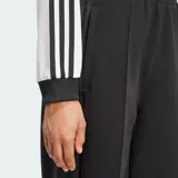 Blusa cropped de manga larga Adidas Adicolor en color blanco, con cuello en V y puños acanalados en negro. Presenta las tres tiras clásicas de la marca en color negro a lo largo de las mangas y el logo del trifolio bordado en el pecho.