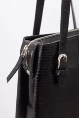 Cartera de hombro estructurada color negro, confeccionada en 100% cuero vacuno con textura en relieve tipo reptil. Cuenta con asas largas ajustables mediante hebillas metálicas plateadas, cierre superior y el logo de la marca grabado en la parte frontal.