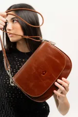 Cartera bandolera de cuero natural color marrón, con estructura rígida, costuras a la vista y logo grabado en el frente.