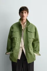 Parka estilo militar color verde, de corte relaxed fit, cuello subido y manga larga. Cuenta con bolsillos de plastrón con solapa en el pecho y en la cadera, cintura ajustable con cordón interior y cierre frontal con cremallera oculta por solapa con botones a presión.