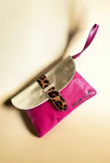 Sobre de mano de cuero fucsia con solapa dorada texturizada, tira de cierre con estampado animal print de leopardo y correa de muñeca fucsia.