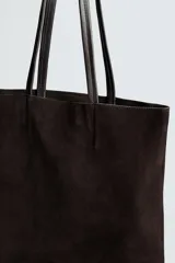 Bolso tipo shopper de diseño minimalista, confeccionado en piel con acabado de serraje. Cuenta con dos asas largas de mano y un compartimento principal espacioso con un bolsillo interior con cierre.
