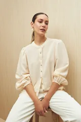 Camisa color crema a rayas verticales, de mangas abullonadas con elástico en los puños, cuello mao y botones de nácar.