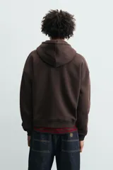 Sudadera con capucha de corte relajado, color marrón oscuro, con interior perchado. Presenta un bolsillo frontal tipo canguro, bordado con la palabra 'LOVE' en el pecho y un parche decorativo a contraste en el bolsillo. Posee puños y ruedo en rib.