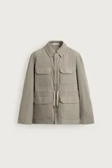 Parka relaxed fit color gris, confeccionada en tejido técnico ligero, con cuello solapa, manga larga con puño abotonado, cuatro bolsillos de plastrón con solapa en el frente, cintura ajustable con cordón y cierre frontal de botones.