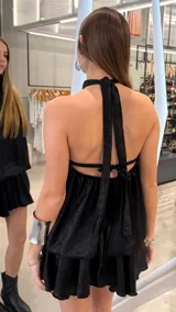 Vestido corto negro de cuello halter con acabado satinado, espalda descubierta y falda evasé con volados.