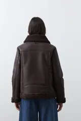 Campera tipo gamulán de símil cuero color marrón oscuro, con interior y solapas de corderito al tono. Presenta cierre frontal cruzado, bolsillos con cierre metálico y hebilla ajustable en el cuello.