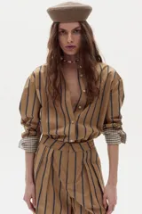 Camisa boxy de popelina de algodón color tostado con diseño de rayas verticales oscuras, cuello camisero, botones frontales y mangas largas con puños estampados a cuadros.