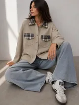 Camisa de tejido de lana color beige, con cuello y bolsillos frontales con solapa en tela a cuadros. Presenta cierre frontal con botones y mangas largas.