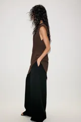 Vestido corto de color marrón, con cuello redondo y diseño sin mangas. Presenta un bajo asimétrico con un lateral más largo y cierre en la espalda con abertura y botón.