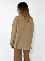 Camisa de corte oversize color beige, con cuello clásico, cierre frontal de botones y detalle de flores de tela aplicadas en el pecho.