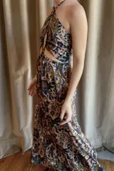 Vestido largo de satén color marrón con estampado de lunares blancos. Presenta un diseño cut-out en la cintura, escote halter con detalle de mostacillas y terminaciones con puntilla negra en el top.
