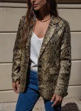 Blazer de corte sastrero con estampado de piel de serpiente en tonos grises y negros. Presenta solapas clásicas, cierre frontal con botones y mangas largas con detalle de botones en los puños.
