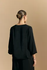 Blusa negra de satén con escote en V y detalle de volados frontales. Presenta mangas largas con puños abotonados y una silueta fluida.