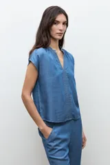 Blusa de lyocell en tono azul medio, con mangas cortas, escote en V y detalles de pespuntes decorativos en la parte frontal.