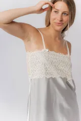 Camisón de satén elastizado color gris claro, con escote recto y detalle de puntilla elastizada en el busto y espalda. Tiene breteles finos regulables y un largo por encima de la rodilla.