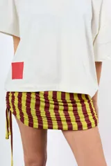 Minifalda de rayas verticales en tonos bordó y beige, confeccionada en tejido elástico con fruncidos laterales regulables mediante cordones.