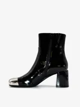 Bota corta de cuero negro con acabado brillante, tacón de bloque y puntera metálica plateada. Cuenta con cierre lateral.