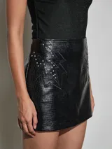 Minifalda negra de cuero sintético con textura efecto reptil, diseño recto y detalles de costuras decorativas con apliques metálicos en los laterales.