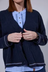 Saco tejido en lambswool con diseño de rombos y trenzas en el frente. Presenta cierre frontal con botones, cuello en V y detalles de rayas en contratono en puños y ruedo. Incluye pin bordado en la manga.