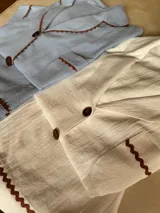 Pijama de algodón color celeste, compuesto por una camisa de manga corta con botones marrones y ribetes festoneados en color marrón, y un short con elástico en la cintura y ribetes festoneados en el ruedo.