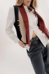 Chaleco abierto de tejido de punto, con diseño de bloques de color verticales en gris claro, negro y gris oscuro. Presenta un cuello ancho tipo chal y un detalle de tres pequeñas aplicaciones bordadas horizontales en tonos verde oliva, naranja quemado y celeste pálido en el frente.