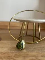 Gargantilla rígida en forma de aro de bronce, con diseño abierto y una piedra natural verde con incrustaciones oscuras montada en uno de los extremos.