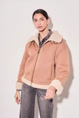 Campera gamulan color rosa con interior de piel sintética color crema, cierre frontal con cremallera y hebillas en el cuello. Corte oversize.