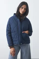 Campera acolchada de nylon color negro, con cuello alto, cierre frontal y botones a presión. Presenta un diseño de rombos y forro interior suave.